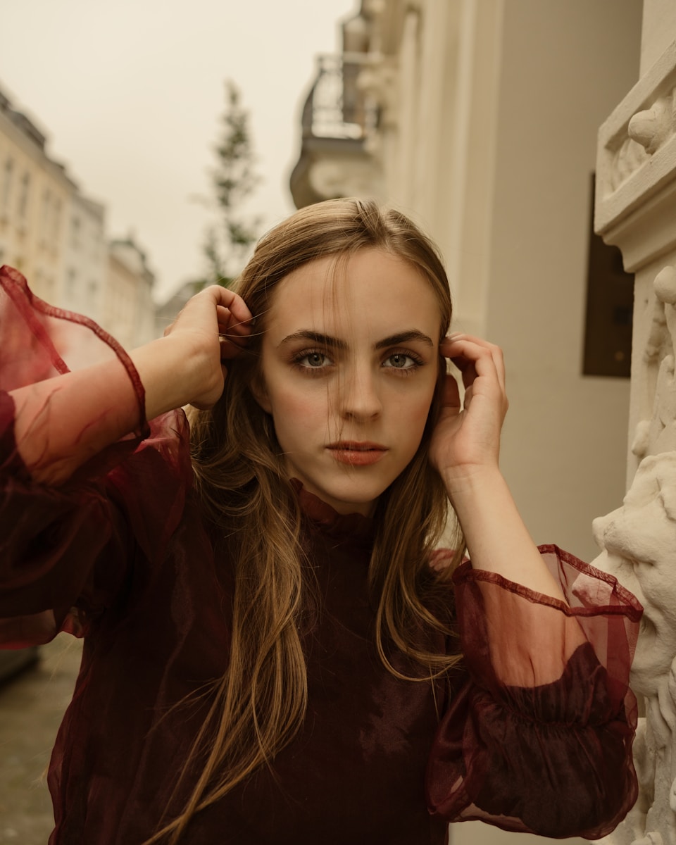 Woman with hands in hair poses in an urban setting.